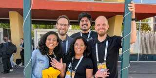 The image has five people standing behind a frame assigned for taking pictures with the conference name to tag it on social media